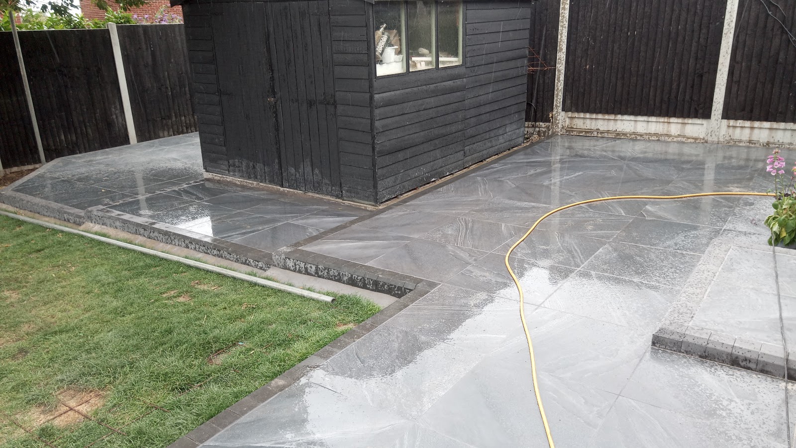 Finished porcelain patio wrapping around a black shed with fresh lawn