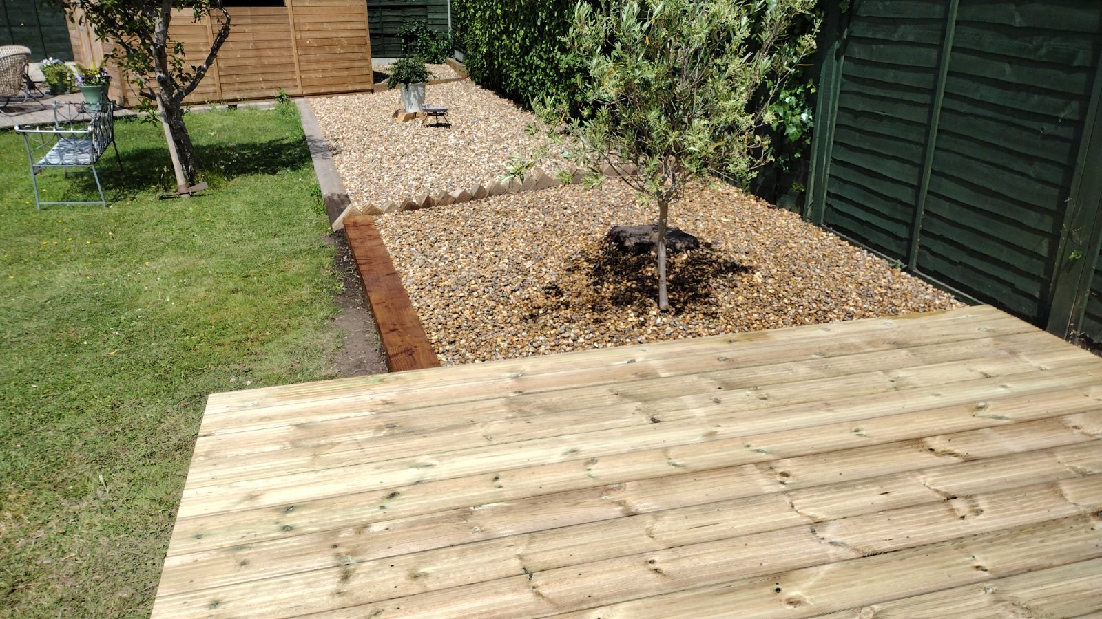 Finished porcelain patio wrapping around a black shed with fresh lawn